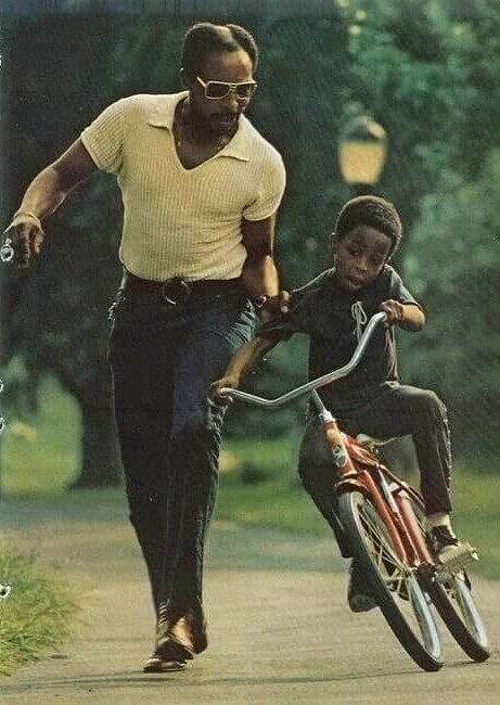 A dad showing his son how to ride a bicycle in Central Park, NYC, circa 1973.